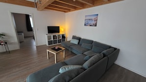 Una sala de estar moderna con un sofá seccional gris, una mesa de centro de madera y un televisor sobre un soporte blanco.