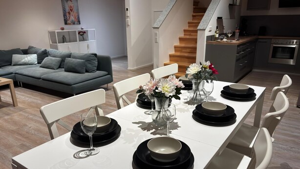 Una mesa de comedor dispuesta con platos negros, sillas blancas y centros de mesa florales.