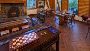 A log cabin interior with a stone fireplace, wooden beams, a chandelier, and a chessboard on a table. - Big Sky Lodge (Ulaanbaatar)