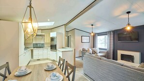 Et moderne køkken med indbyggede apparater, et spiseområde med et træbord og stole, samt en opholdsstue med sofa og pejs.