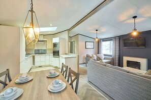 A modern kitchen with built-in appliances, a dining area with a wooden table and chairs, and a living area with a sofa and fireplace. - Host & Stay | POR01 Lotus Lodge (Pocklington)
