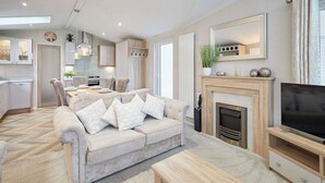 Een moderne woonkamer met een bank, salontafel, open haard, televisie en keukenhoek.