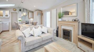 A modern living room with a sofa, coffee table, fireplace, TV, and kitchen area.