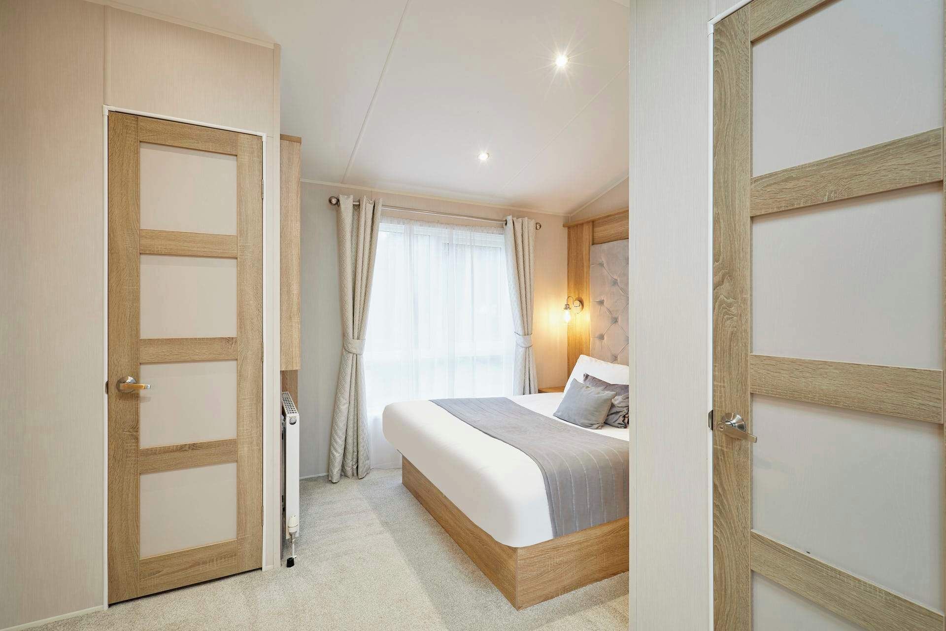 Une chambre à coucher comprenant un lit, une table de chevet, une lampe fixée au mur et une fenêtre avec des rideaux.
