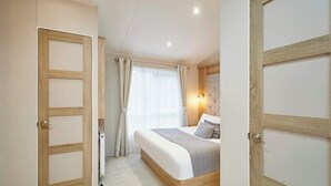 Een slaapkamer met een bed, nachtkastje, een wandlamp en een raam met gordijnen.