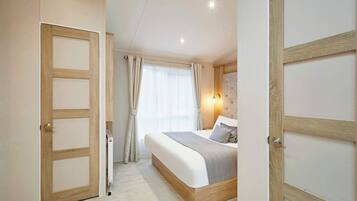 Une chambre à coucher comprenant un lit, une table de chevet, une lampe fixée au mur et une fenêtre avec des rideaux.
