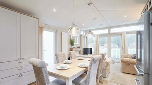 Een moderne keuken met een eethoek, met een houten tafel, grijze gestoffeerde stoelen, hanglampen en een ingebouwde televisie.