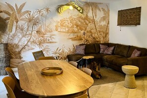Un salon avec une fresque murale, un canapé marron, une table à manger en bois et un arbre à chat.