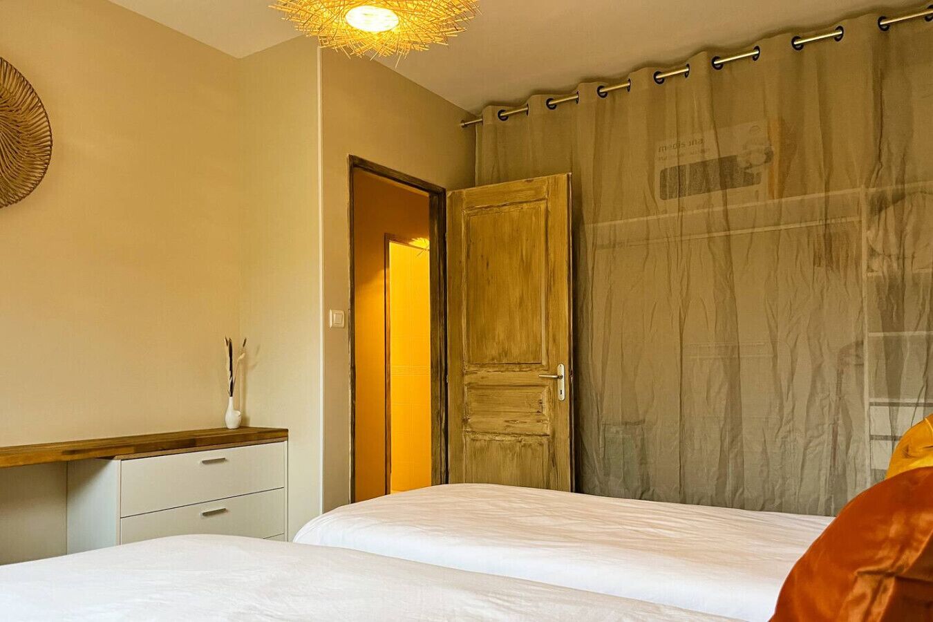 Une chambre à coucher avec un lit, une armoire en bois, une table de chevet avec un vase et un rideau.
