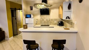Una cucina compatta con isola centrale, due sgabelli da bar, una macchina da caffè e un lampadario decorativo.