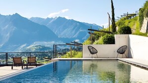 A swimming pool with a view of mountains, two lounge chairs, and a modern chair. - Pratenberg Apartment Weite Penthouse with Mountain View, Sauna & Saltwater Rooftop Pool (Merano)