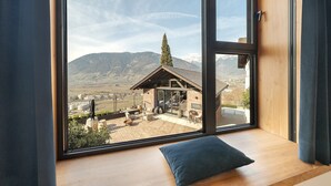 A room with a large window overlooking a mountainous landscape, a wooden bench, and a small outdoor seating area. - Pratenberg Apartment Weite Penthouse with Mountain View, Sauna & Saltwater Rooftop Pool (Merano)