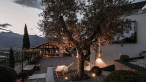 Un edificio con un espacio de estar al aire libre cubierto, un árbol y una montaña al fondo.
