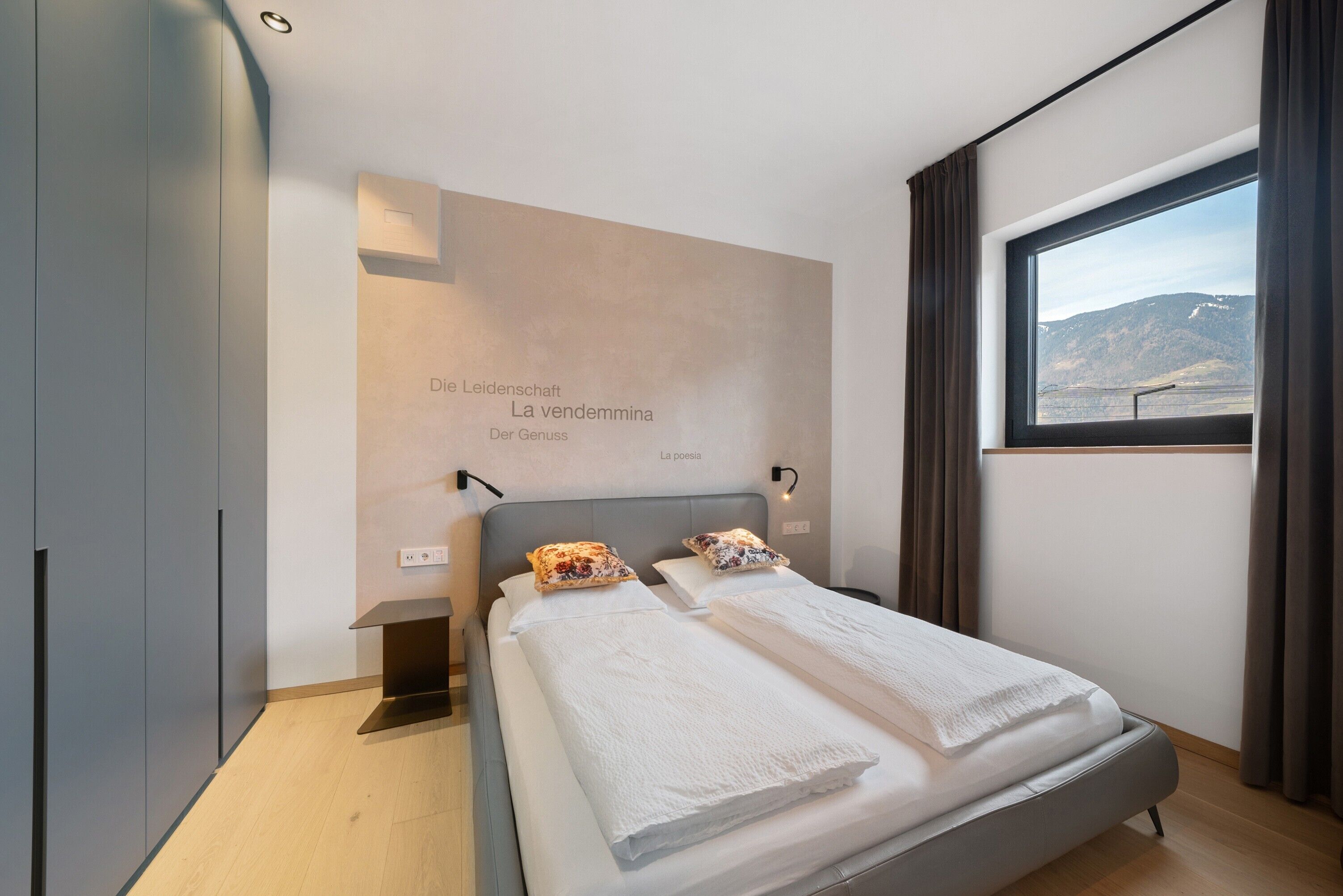 Une chambre moderne comprenant un lit, une table de chevet, une lampe fixée au mur, une fenêtre avec vue et une armoire.