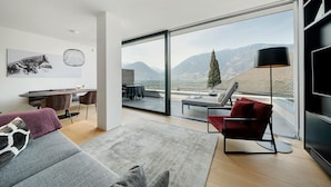 A modern living room with a sofa, a red chair, a desk, and a large window with a mountain view. - Pratenberg Apartment 'Bordeaux Penthouse' with Mountain View, Sauna & Rooftop Saltwater Pool (Merano)