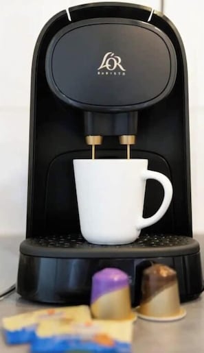 Eine Kaffeemaschine mit einem weißen Becherhalter und zwei Kaffeekapseln darunter.