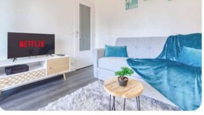 Un soggiorno moderno con un divano grigio, una televisione a schermo piatto, un tavolino da caffè in legno con una pianta e una porta bianca.