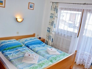 A double bed with blue and green bedding, a nightstand with a lamp, and a window with sheer curtains. - Rosskopf by Interhome (Wildschönau)