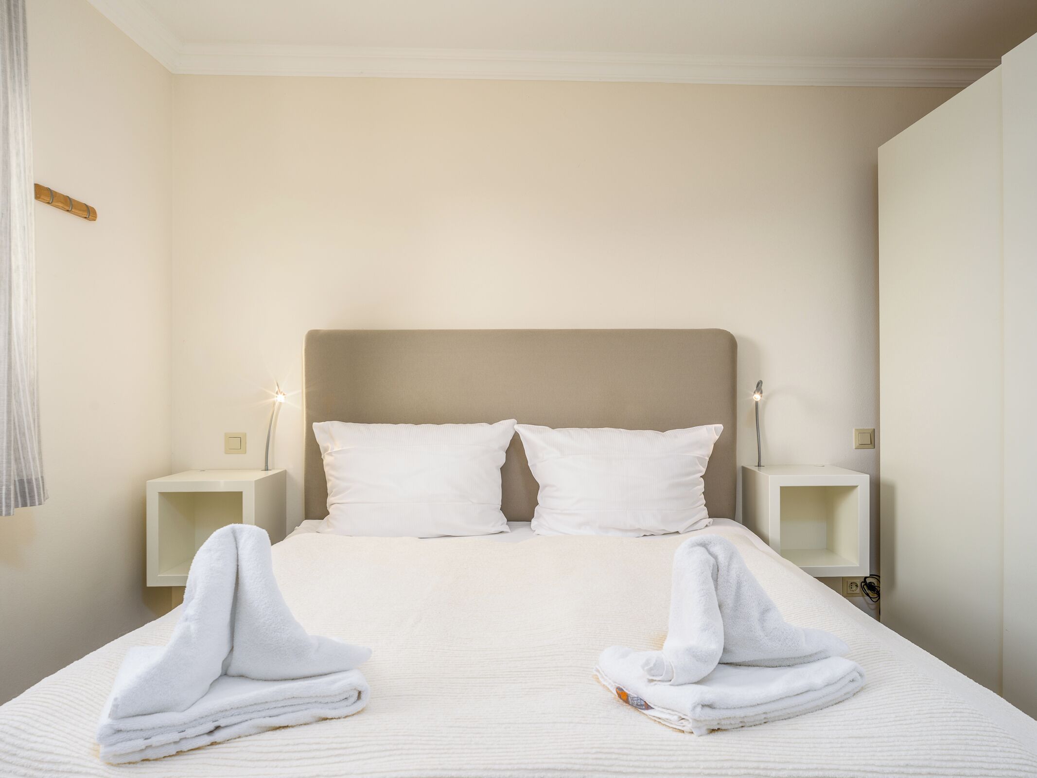Un lit bien fait, avec deux oreillers, deux tables de chevet avec des lampes et des serviettes pliées posées sur le lit.