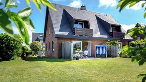 A two-story house with a sloped roof, a visible front door, and a small patio area with outdoor furniture. - Owl's Nest - Wenningstedt-Braderup (Sylt) (Wenningstedt-Braderup (Sylt))
