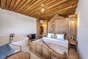 A room with a wooden ceiling, a large bed with a decorative headboard, a bathtub, and a mirror with intricate designs. - Tol Of Cappadocia (Nevsehir)