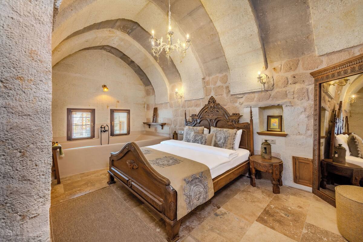 A bedroom with a large bed, stone walls, a chandelier, and a mirror.