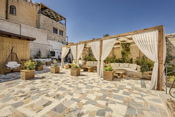 An outdoor patio with stone flooring, wooden furniture, and a covered seating area with curtains. - Tol Of Cappadocia (Nevsehir)