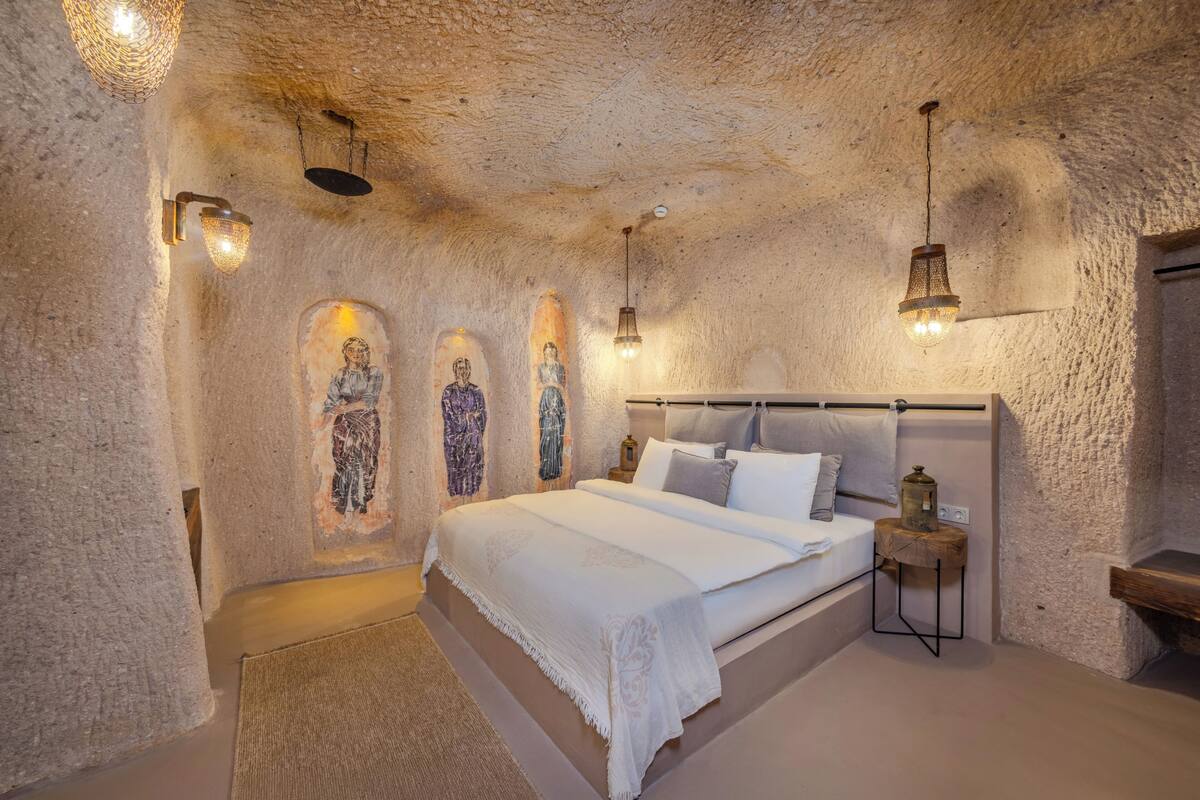 A bedroom with a stone wall, a bed with white bedding, a nightstand, and wall-mounted lights.