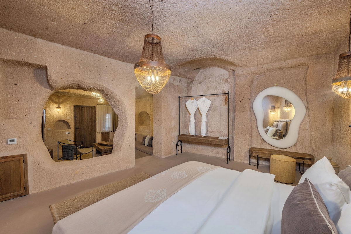 A room with a large bed, a hanging light fixture, a mirror, and a wooden bench.