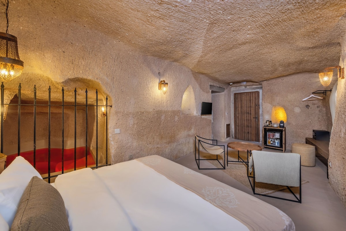 A cozy, cave-like room with a bed, a chair, a small table, and a television.