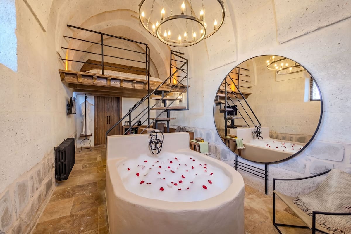 A bathroom with a large bathtub, a round mirror, a chandelier, and a staircase.