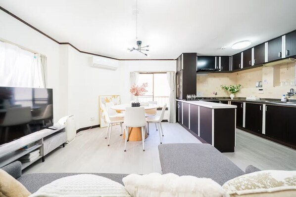 A modern living room with a flat-screen TV, a sofa, and a dining area with a table and chairs.