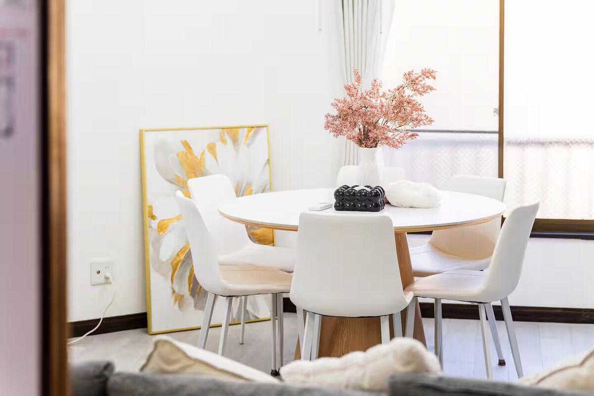 A modern dining area with a round table, white chairs, and a vase with pink flowers.