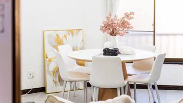 A modern dining area with a round table, white chairs, and a vase with pink flowers.
