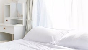 Un lit bien fait, avec du linge de lit blanc, dans une chambre lumineuse où se trouvent une commode blanche et un miroir.