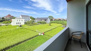 Un balcone con vista su un campo verde, una sedia e un edificio sullo sfondo.
