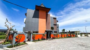 Un edificio moderno con una facciata imponente in arancione e grigio, un tetto piano e un'area d'ingresso pavimentata.