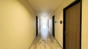 Un corridoio d'hotel con pavimento in marmo, porte su entrambi i lati e un lampadario a soffitto.