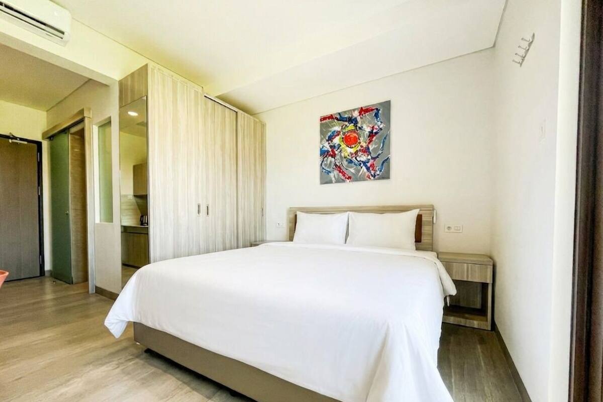 Una habitación de hotel con una cama, una mesita de noche, un cuadro y una puerta que da a un baño.