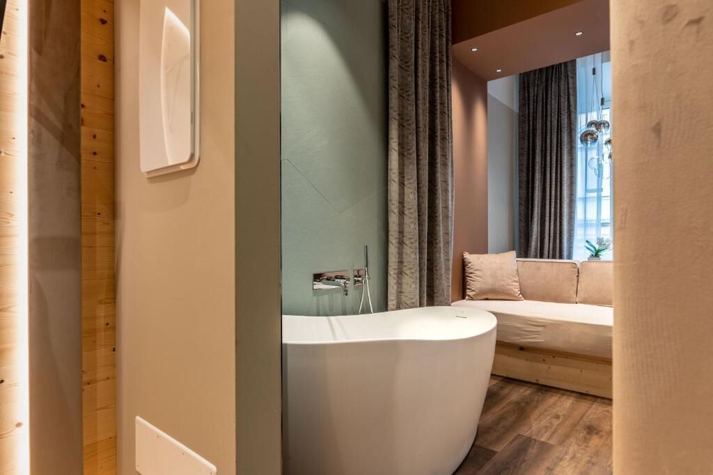 Un baño moderno con una bañera independiente, suelo de madera y ventana con cortinas.