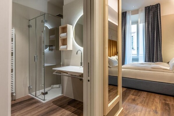 A modern bedroom with a glass shower enclosure, a bedside table with a mirror, and a bed with a dark headboard.