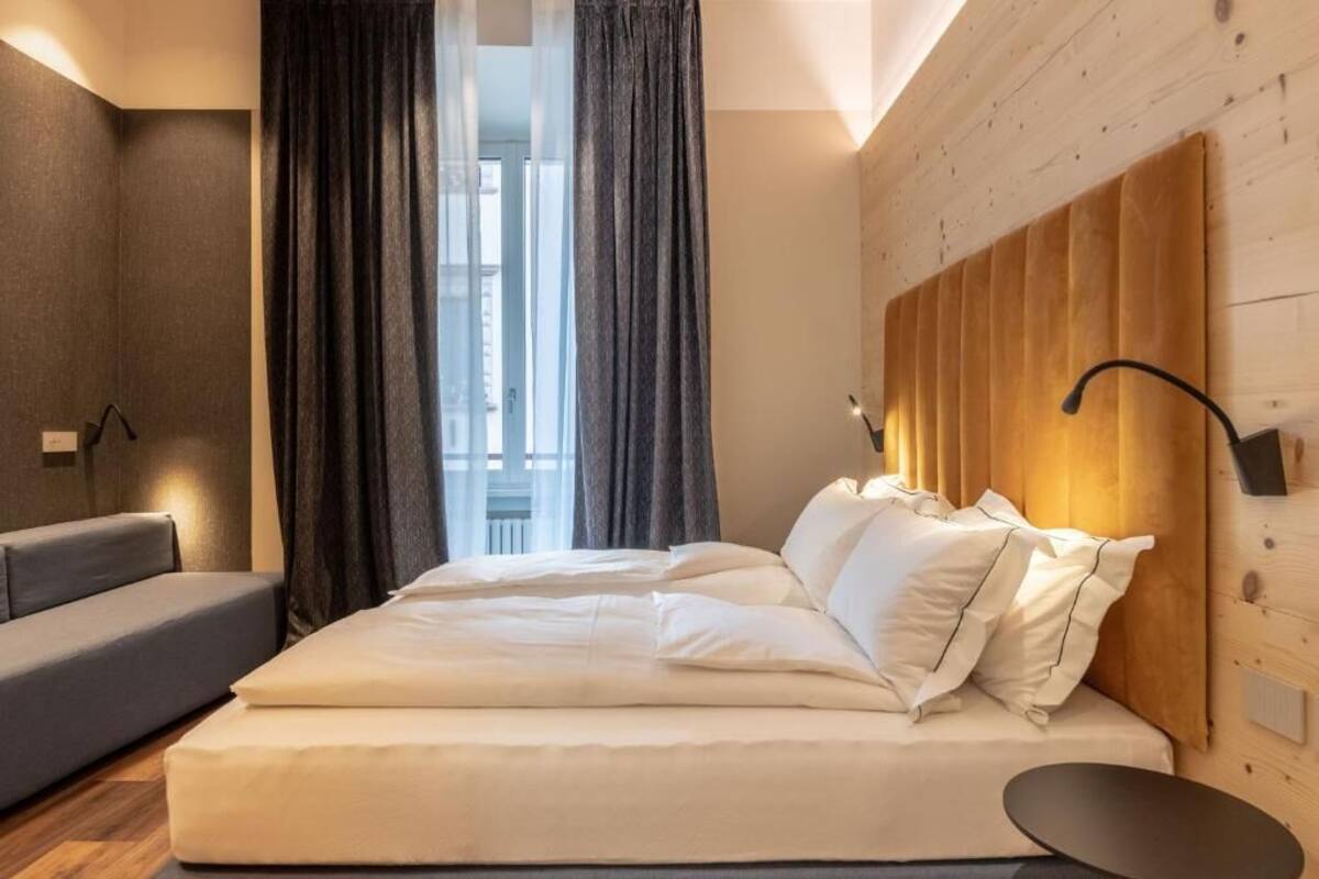 A bedroom with a bed, a sofa, a window with curtains, and a wooden headboard.