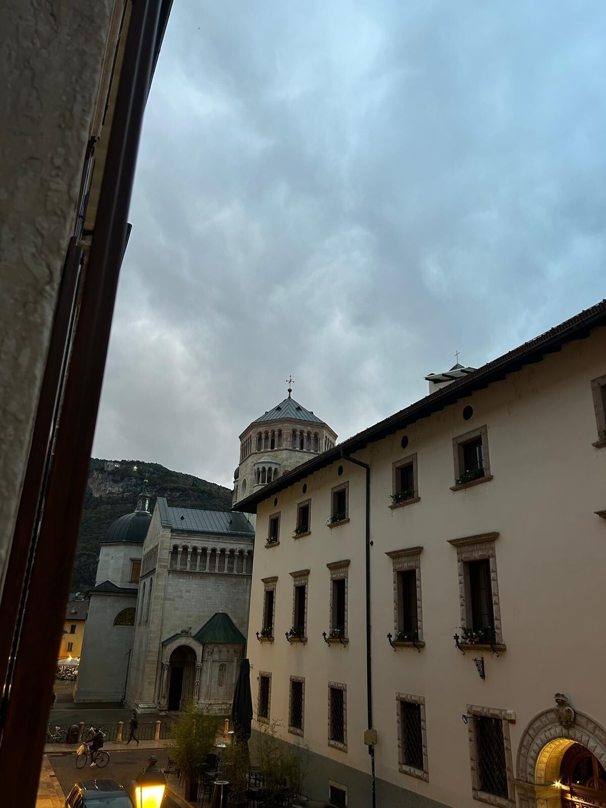 Vista de un edificio con cúpula y campanario, una calle con un ciclista y una montaña al fondo.