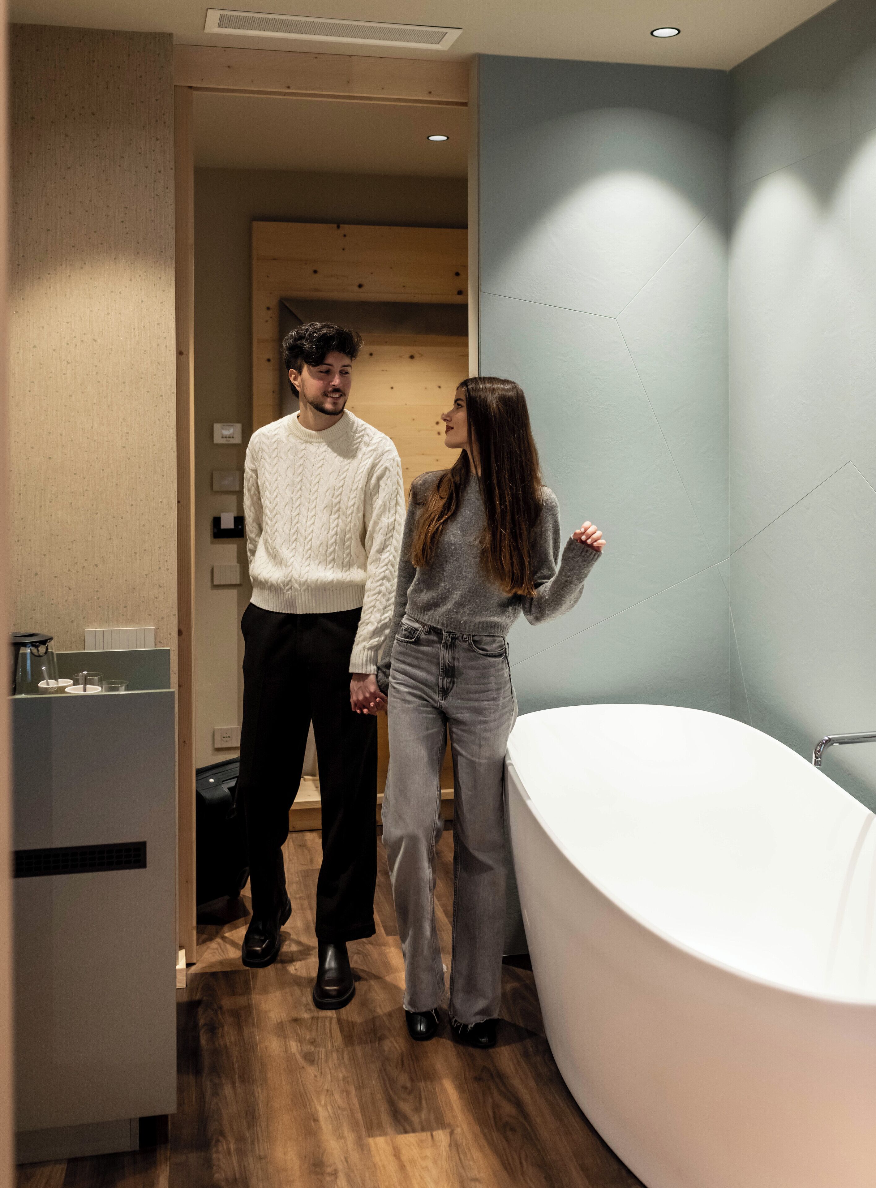 Un baño moderno con una bañera grande, suelo de madera y pared azul claro.