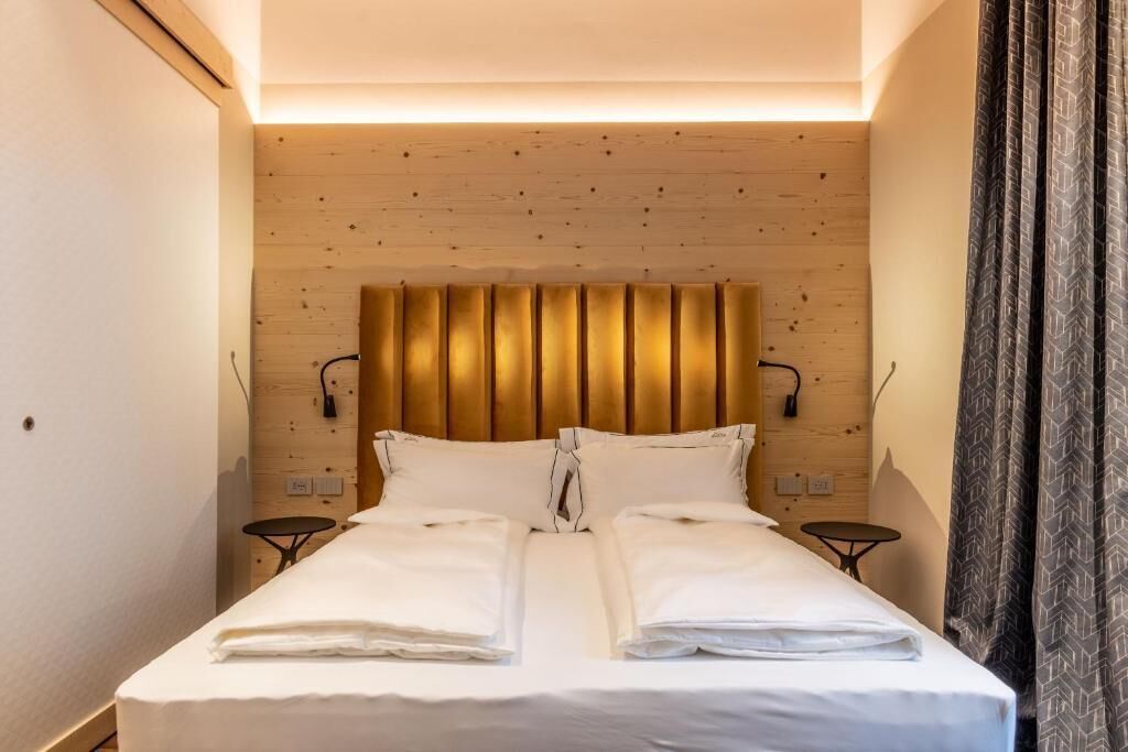 Quarto de hotel com cabeceira de madeira, duas mesas de cabeceira e cama com roupa de cama branca.