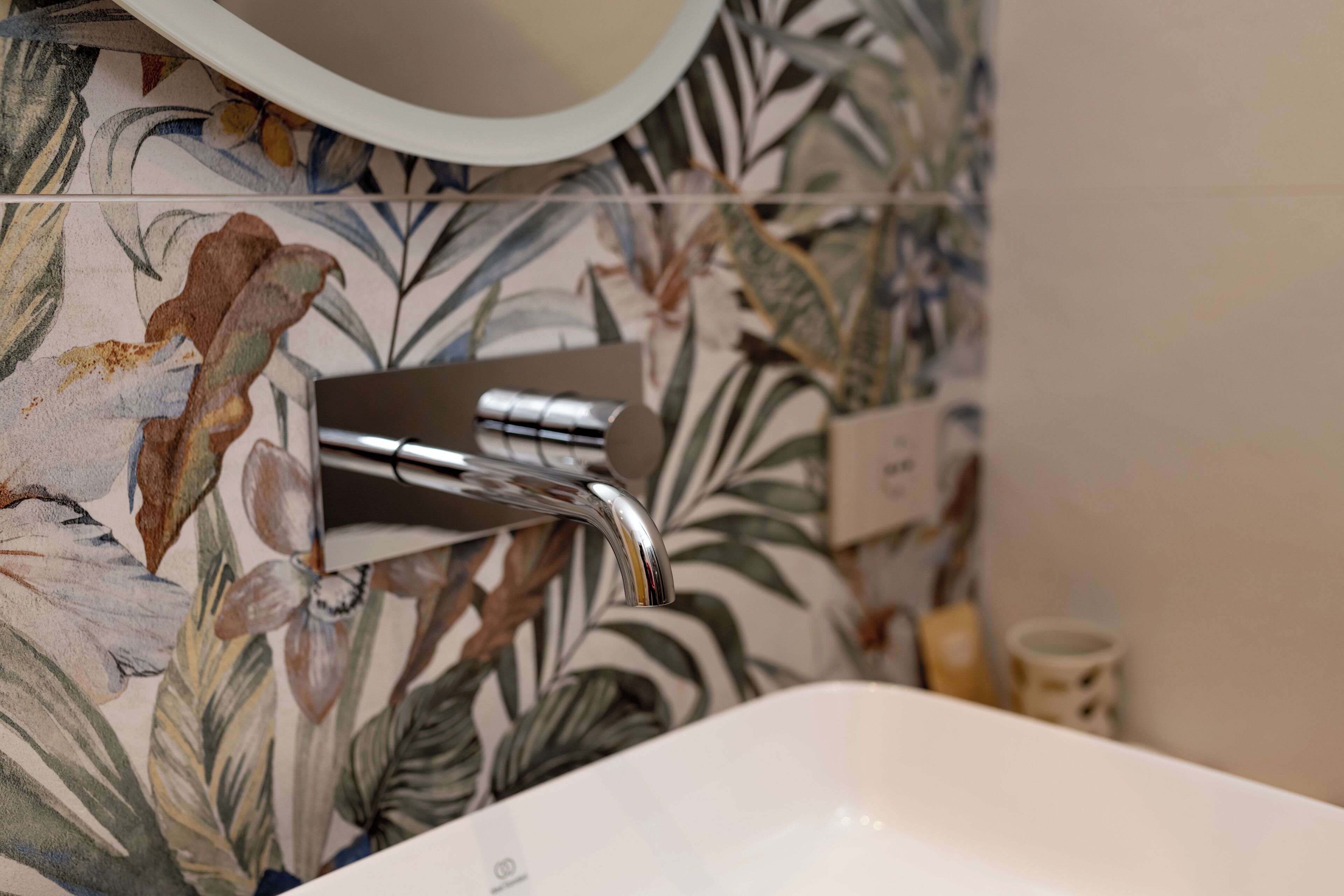 A bathroom with a white sink, a chrome faucet, and a floral-patterned wall.