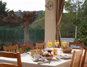 Ein Frühstückstisch im Freien mit Blick auf Baum und Hecke.