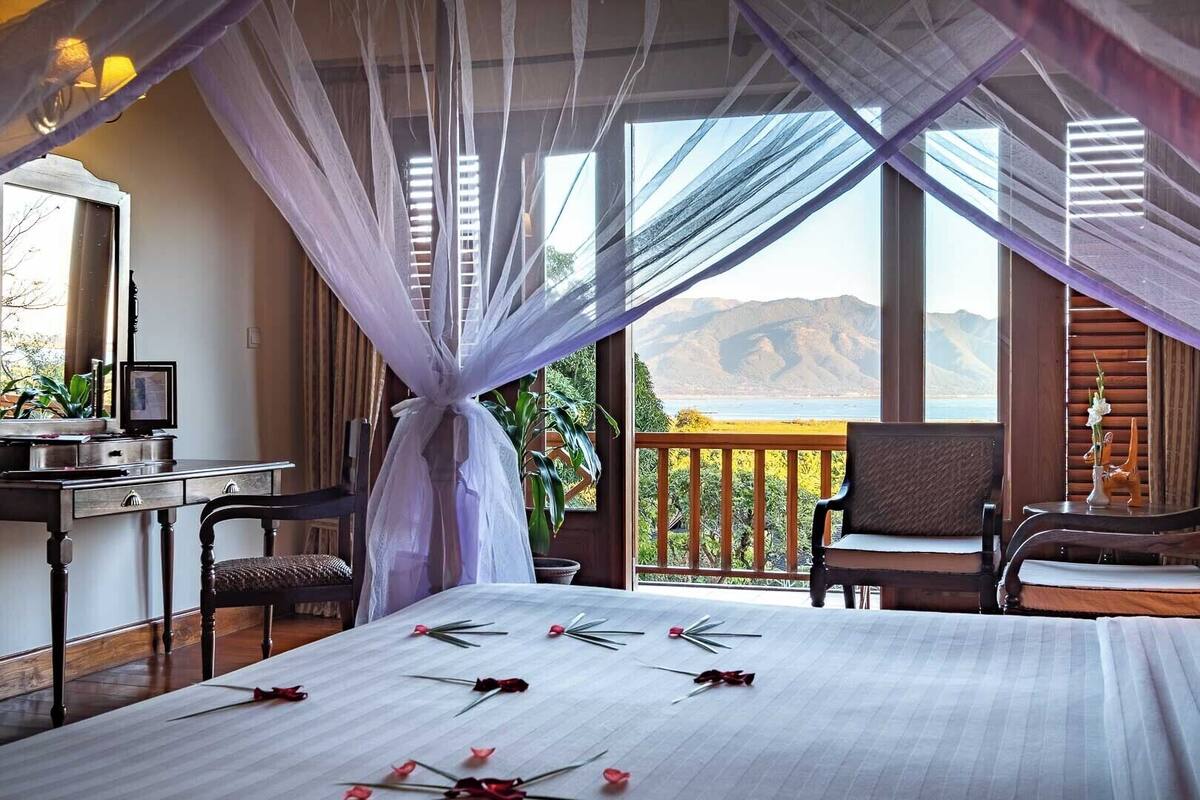 Un dormitorio con cama, escritorio y silla. Hay un balcón con vistas a las montañas.