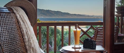 A balcony with a view of the sea, a chair, a table with a drink, and a camera.