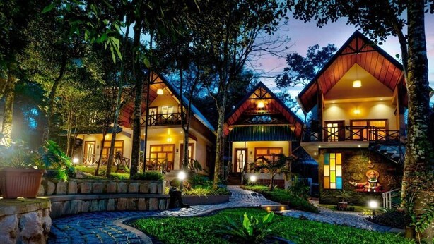 A row of wooden cabins with balconies, surrounded by lush greenery and a stone pathway. - Casa Bella Resort Thekkady (Kumily)